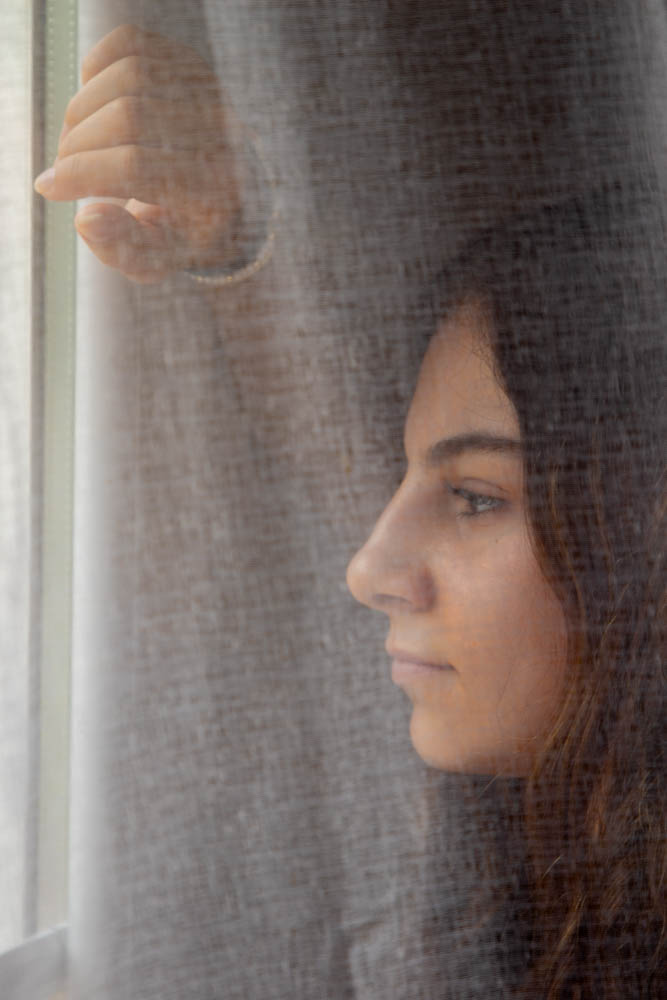 image regardant dehors par la fenetre derriere un voile